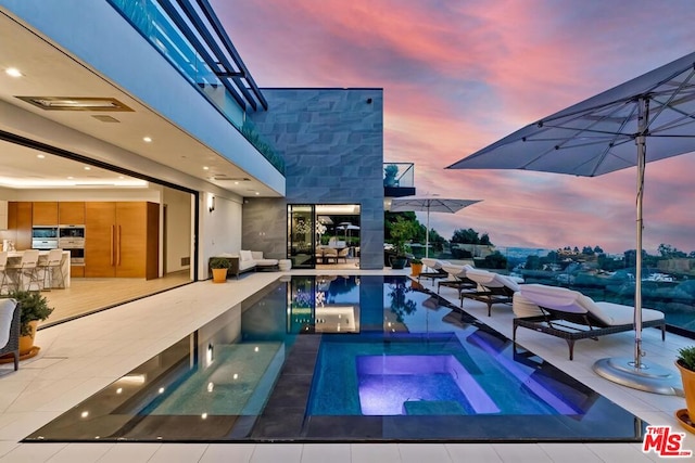 pool at dusk with a patio and an in ground hot tub