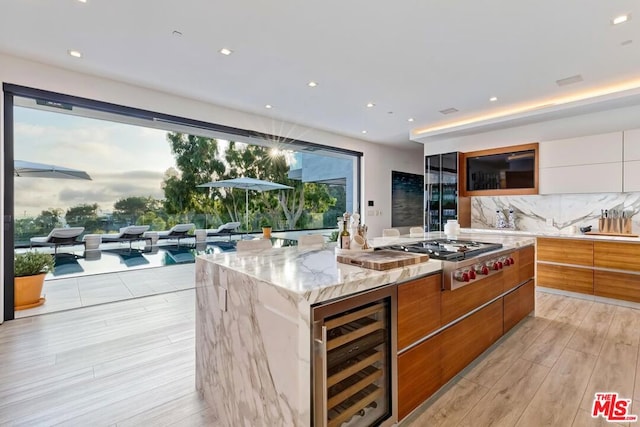 kitchen featuring light wood-type flooring, a large island with sink, beverage cooler, white cabinets, and stainless steel gas cooktop