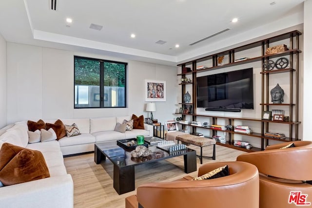 living room with light wood-type flooring and a tray ceiling