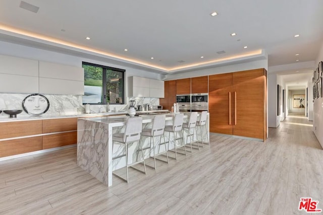 kitchen with a spacious island, a breakfast bar area, light hardwood / wood-style flooring, and white cabinetry