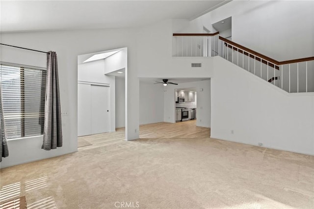 unfurnished living room featuring ceiling fan, a towering ceiling, and light carpet