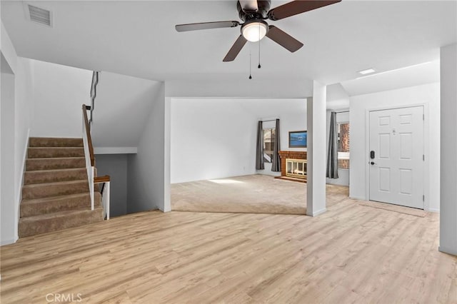 unfurnished living room featuring ceiling fan, a brick fireplace, and light wood-type flooring