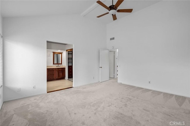 unfurnished bedroom with sink, beam ceiling, high vaulted ceiling, connected bathroom, and light colored carpet