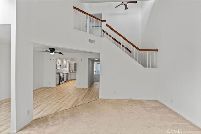 unfurnished living room featuring a towering ceiling, ceiling fan, and carpet flooring