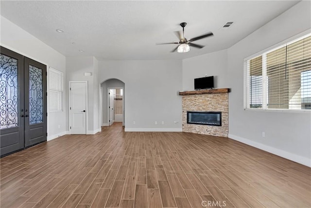 unfurnished living room with a fireplace, french doors, light wood-type flooring, and ceiling fan