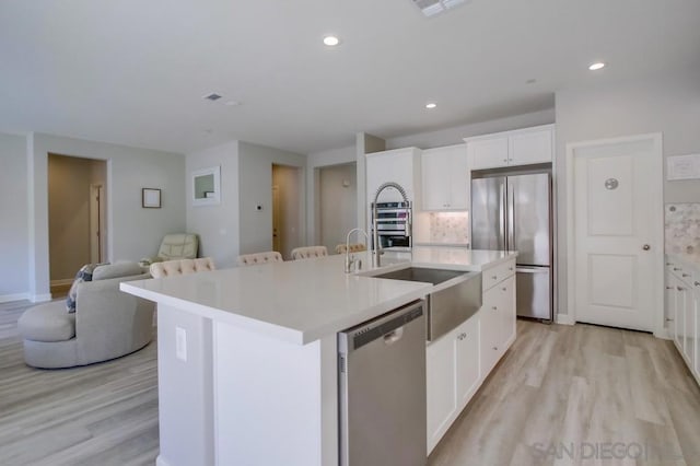 kitchen with white cabinetry, appliances with stainless steel finishes, a center island with sink, and light hardwood / wood-style flooring