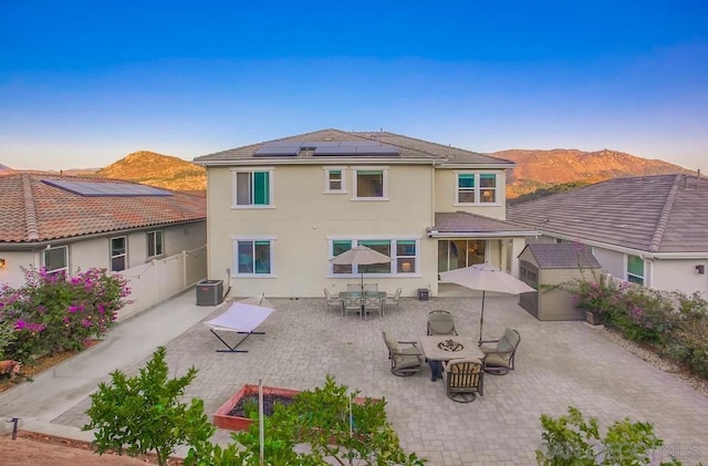 back house at dusk featuring central AC unit, a mountain view, a patio, and solar panels