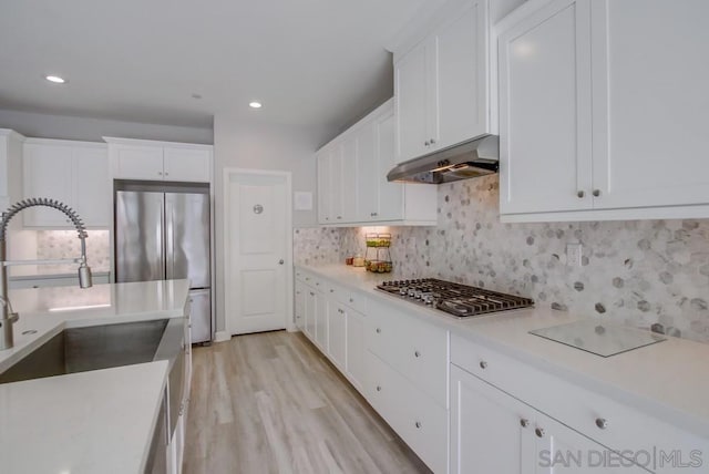 kitchen featuring sink, appliances with stainless steel finishes, backsplash, white cabinets, and light wood-type flooring