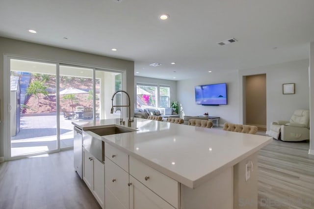 kitchen with white cabinetry, sink, a kitchen island with sink, stainless steel dishwasher, and light hardwood / wood-style floors