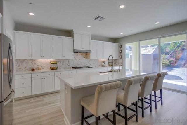 kitchen with sink, white cabinets, stainless steel fridge, a kitchen island with sink, and gas stovetop