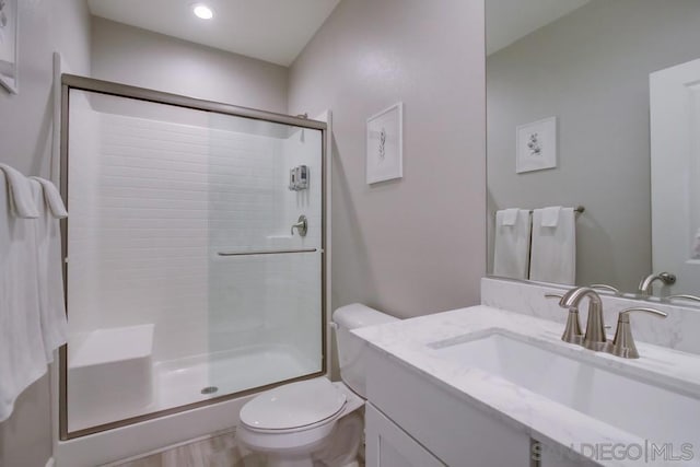 bathroom featuring a shower with door, vanity, and toilet