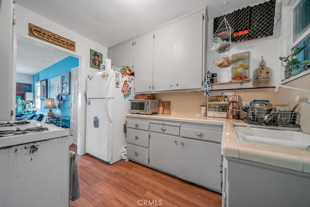 kitchen with white cabinetry, sink, white fridge, and light wood-type flooring