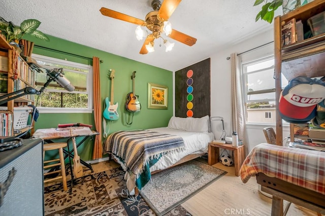 bedroom with multiple windows, a textured ceiling, wood-type flooring, and ceiling fan