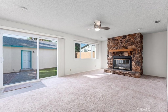 unfurnished living room featuring ceiling fan, carpet, a textured ceiling, and a stone fireplace