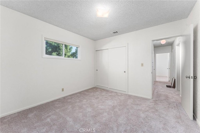 unfurnished bedroom with light colored carpet, a textured ceiling, and a closet