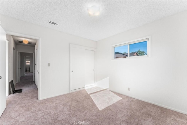 unfurnished bedroom featuring baseboards, visible vents, a textured ceiling, carpet flooring, and a closet