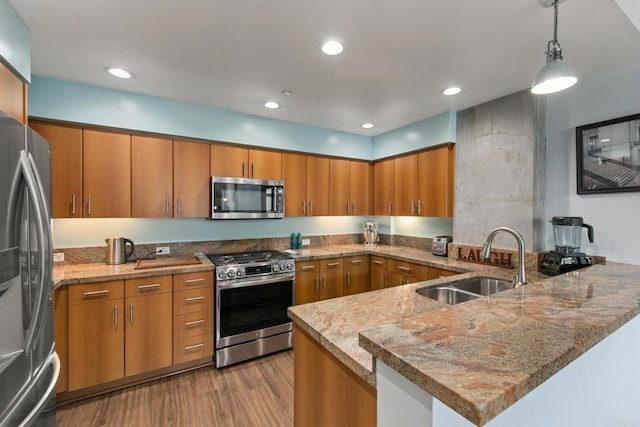 kitchen with brown cabinetry, decorative light fixtures, a peninsula, stainless steel appliances, and a sink