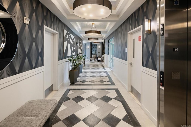 corridor featuring wallpapered walls, a raised ceiling, wainscoting, elevator, and a decorative wall