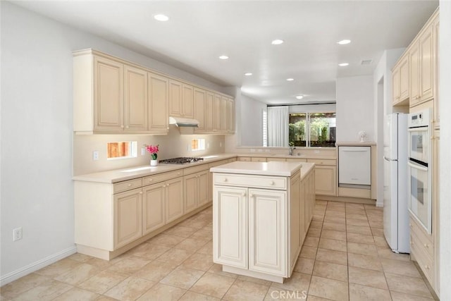 kitchen with white appliances, sink, cream cabinets, light tile patterned floors, and a kitchen island