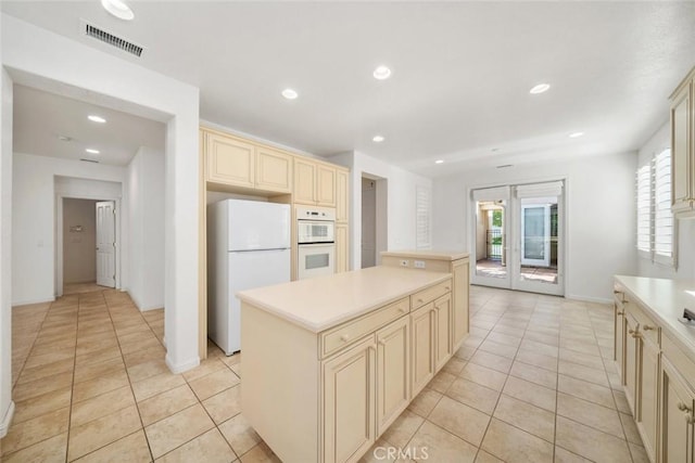 kitchen featuring cream cabinetry, a kitchen island, white appliances, and light tile patterned floors