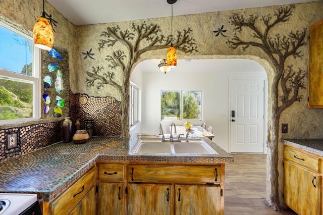 kitchen featuring light wood-type flooring, kitchen peninsula, decorative light fixtures, and sink