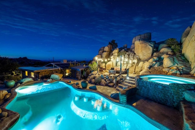 pool at night with a patio and an in ground hot tub