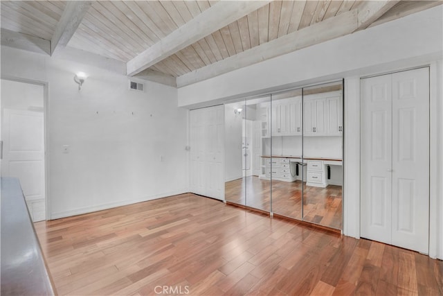 unfurnished bedroom with built in desk, light hardwood / wood-style floors, beamed ceiling, and wooden ceiling