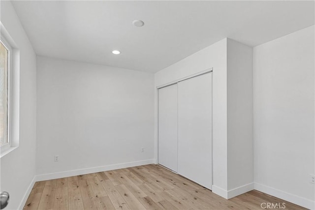 unfurnished bedroom with light wood-type flooring, a closet, and multiple windows