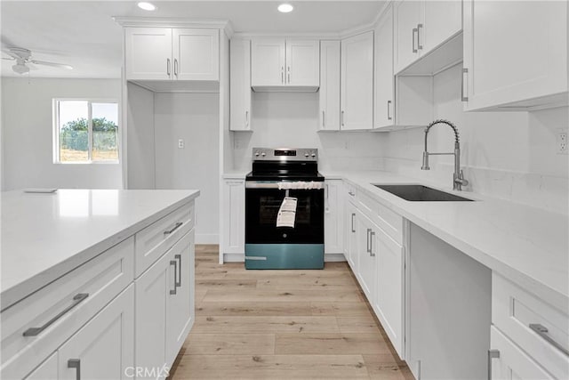 kitchen with stainless steel electric stove, white cabinets, sink, ceiling fan, and light hardwood / wood-style floors