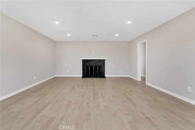 unfurnished living room featuring light wood-type flooring and a brick fireplace