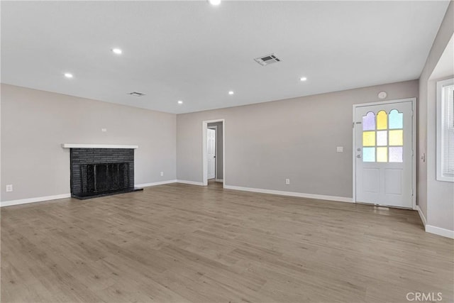 unfurnished living room with a brick fireplace and light wood-type flooring