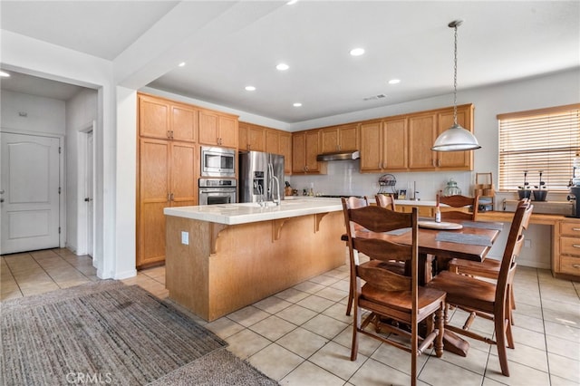 kitchen featuring light tile patterned floors, an island with sink, tasteful backsplash, decorative light fixtures, and stainless steel appliances