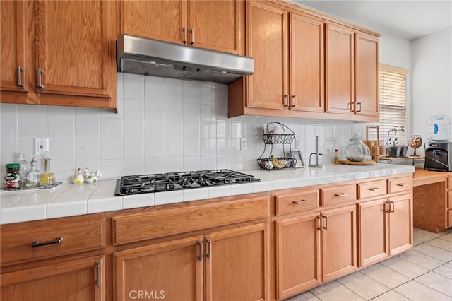 kitchen featuring backsplash, tile counters, light tile patterned floors, and stainless steel gas stovetop