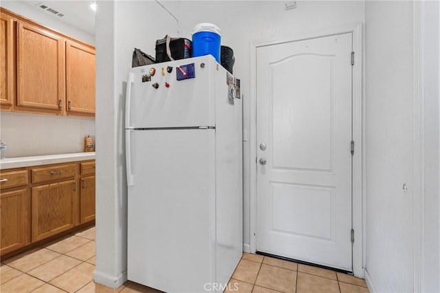 kitchen featuring decorative backsplash, light tile patterned floors, and white fridge