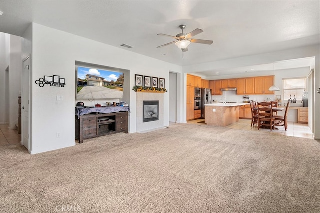 carpeted living room with ceiling fan and a tiled fireplace