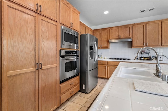 kitchen featuring decorative backsplash, stainless steel appliances, sink, light tile patterned floors, and tile countertops