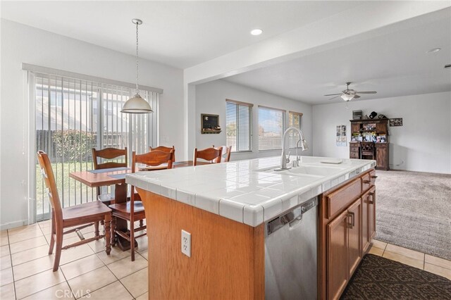 kitchen with stainless steel dishwasher, a kitchen island with sink, sink, decorative light fixtures, and tile counters