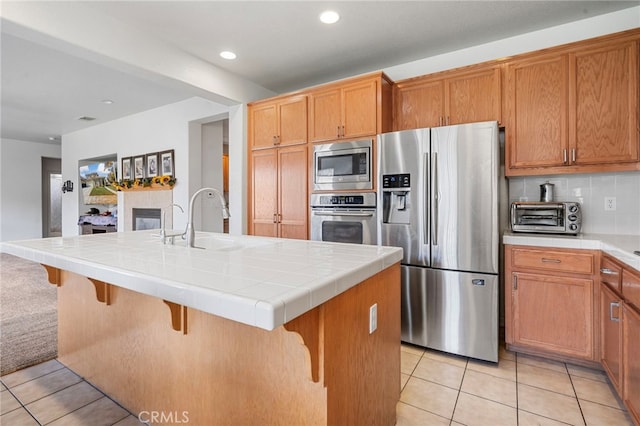 kitchen with tile counters, sink, an island with sink, and appliances with stainless steel finishes