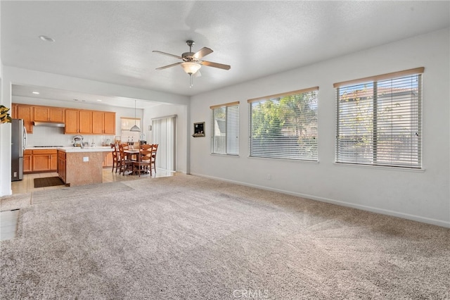 unfurnished living room featuring ceiling fan, light colored carpet, and a textured ceiling