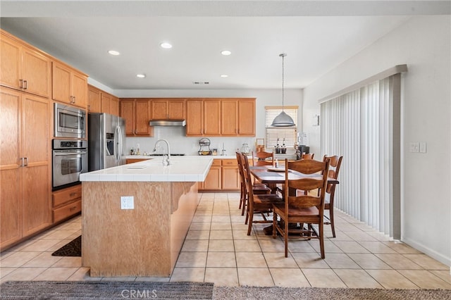 kitchen featuring appliances with stainless steel finishes, light tile patterned floors, tile countertops, decorative light fixtures, and an island with sink