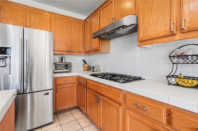 kitchen with stainless steel fridge, tasteful backsplash, light tile patterned floors, tile countertops, and black gas cooktop