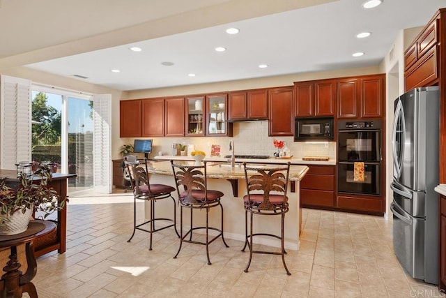 kitchen with light stone counters, a kitchen island with sink, decorative backsplash, black appliances, and a kitchen bar