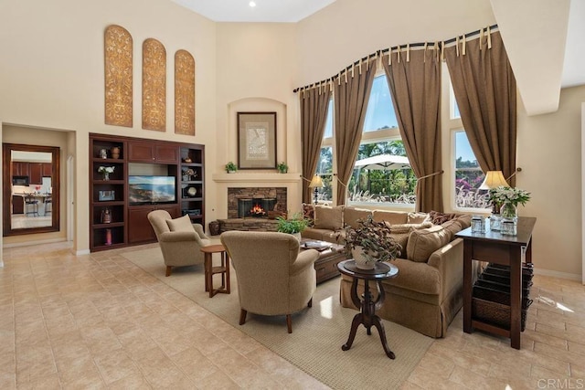 sitting room featuring a stone fireplace, a high ceiling, and baseboards