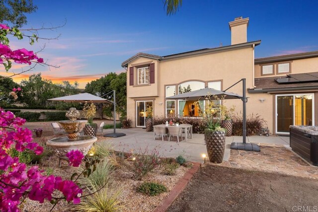 back of house at dusk featuring a chimney, a patio area, and stucco siding