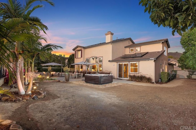 back of house at dusk featuring stucco siding, a chimney, an outdoor hangout area, and a patio