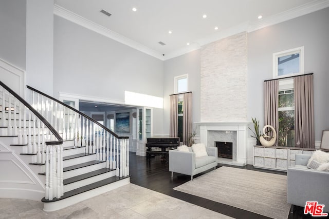 living room featuring a high ceiling, hardwood / wood-style flooring, a fireplace, and crown molding