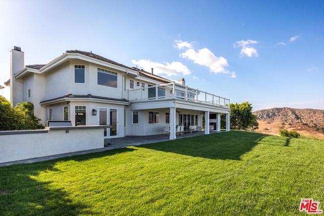 rear view of property with a mountain view, a balcony, a yard, and a patio