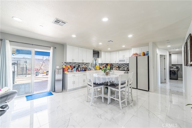 kitchen with decorative backsplash, white cabinetry, white appliances, a kitchen island, and washer / dryer