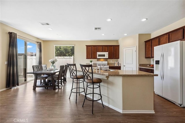 kitchen featuring white appliances, a kitchen island with sink, dark wood-type flooring, sink, and a kitchen bar