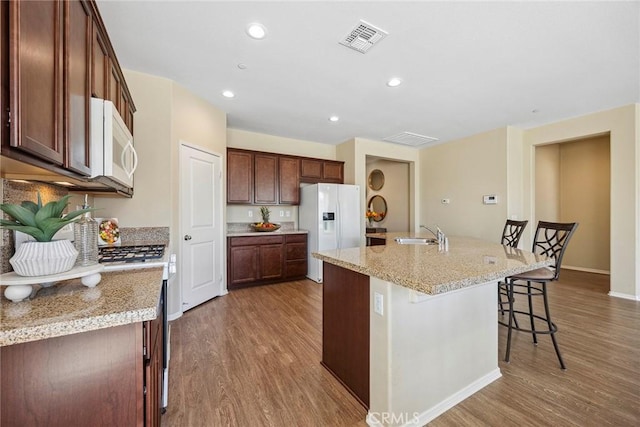 kitchen featuring light stone counters, hardwood / wood-style floors, an island with sink, white appliances, and a kitchen bar